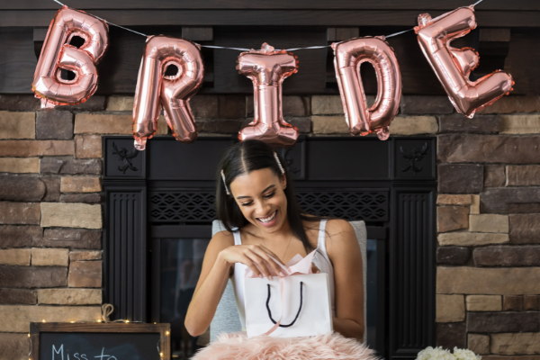 bride opening up bridal shower gifts in front of "Bride" balloons